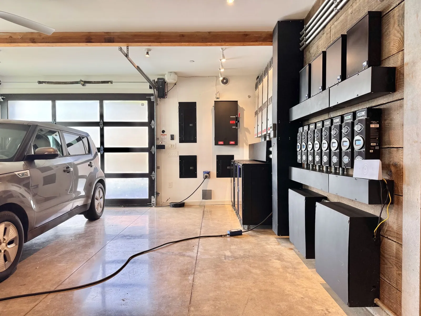 Wide view of the garage from the opposite angle: polished concrete floor, exposed wood beam, and the off-grid power system along the far wall