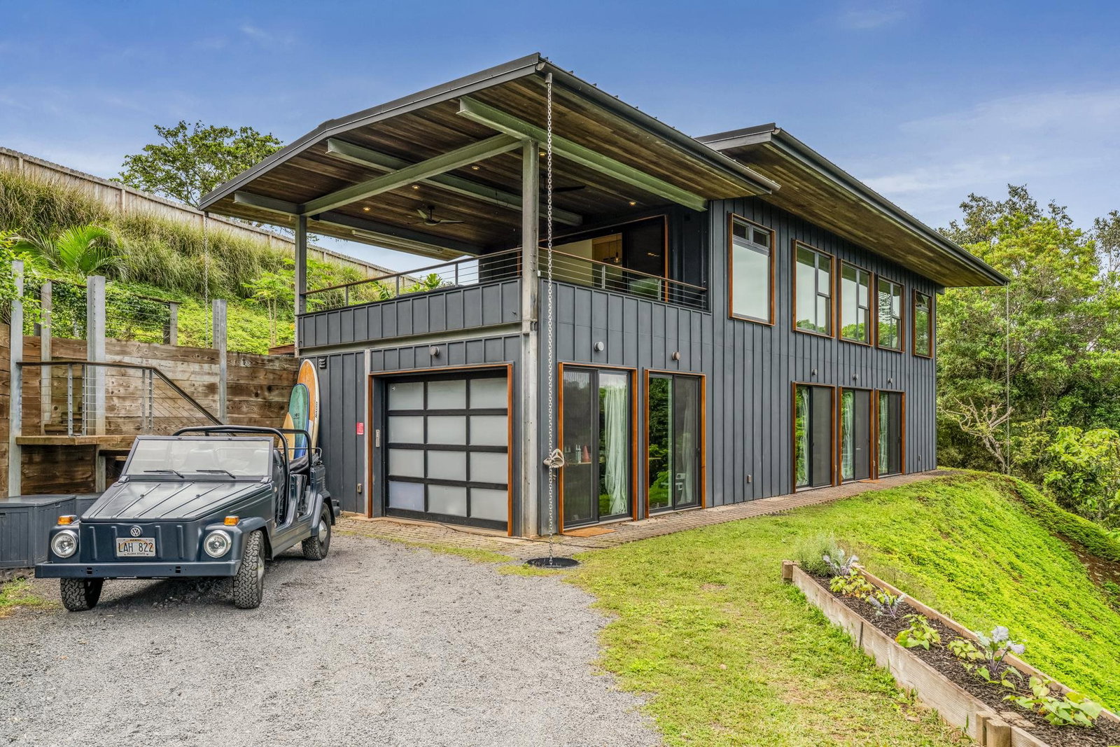 The house by day, black cladding against the jungle, a 1974 Volkswagen Thing in the driveway