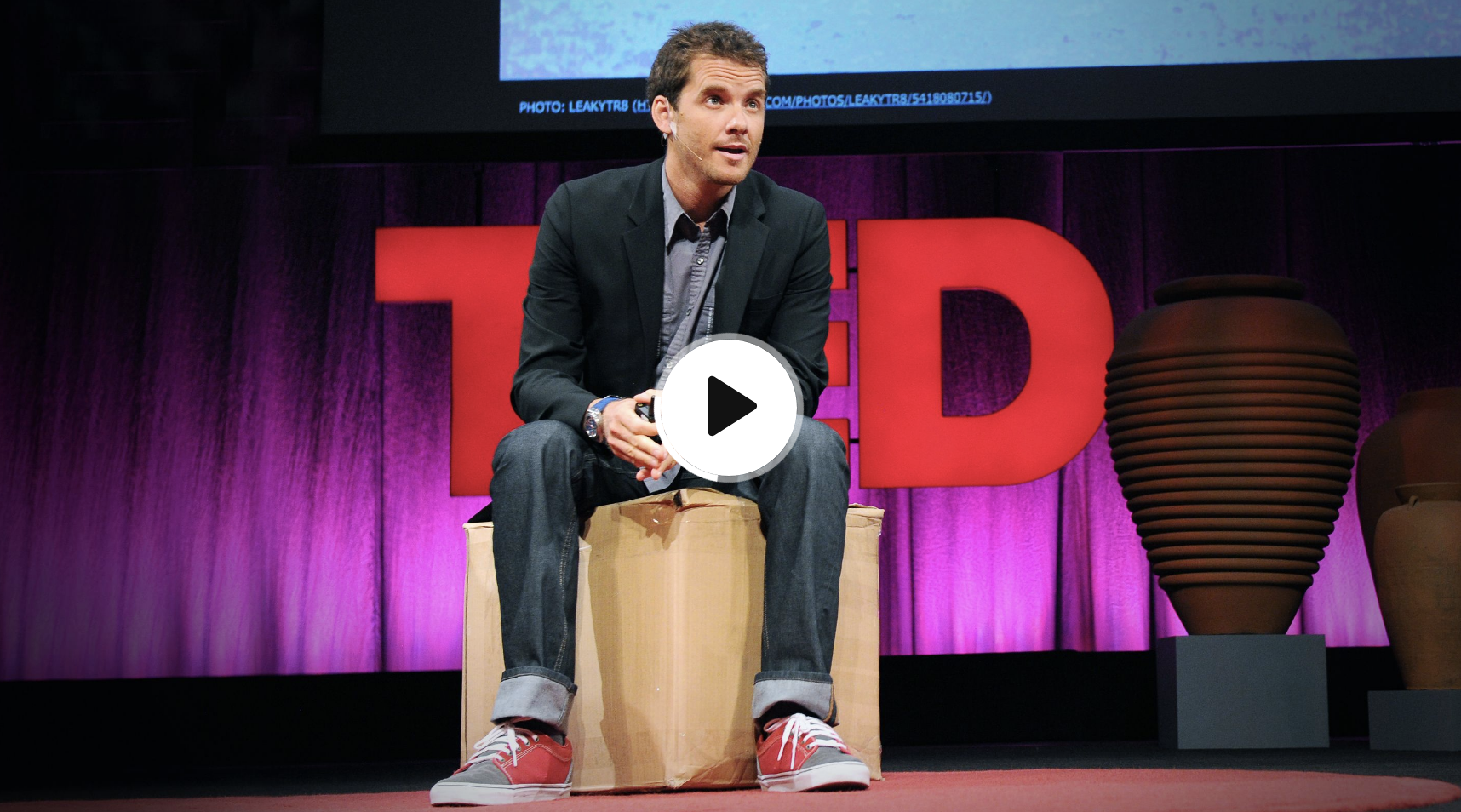 Graham Hill on the TED mainstage, seated on cardboard boxes in front of the red TED logo