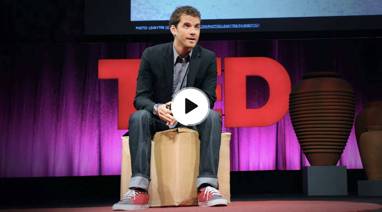 Graham Hill on the TED mainstage, seated on cardboard boxes in front of the red TED logo